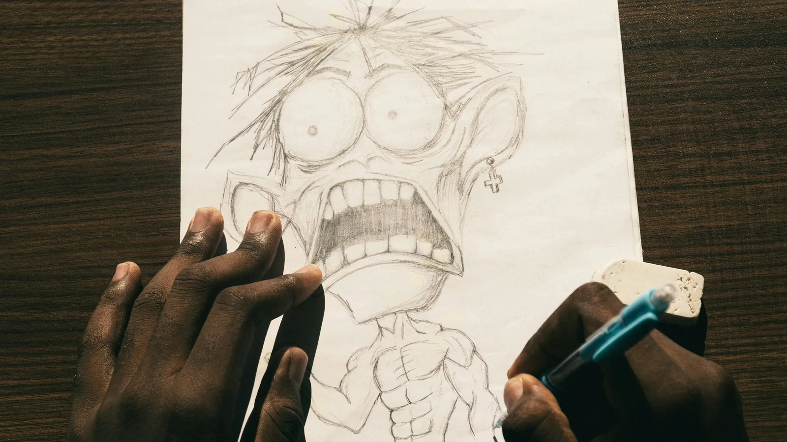 Manos dibujando a lápiz un personaje de caricatura con ojos grandes sobre una hoja blanca